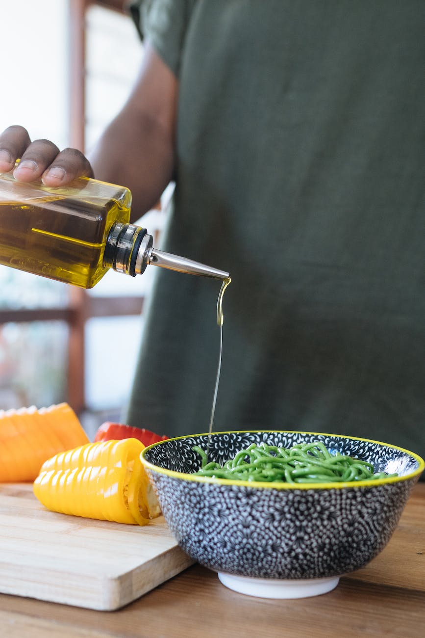 person pouring liquid on green noodles in ceramic bowl